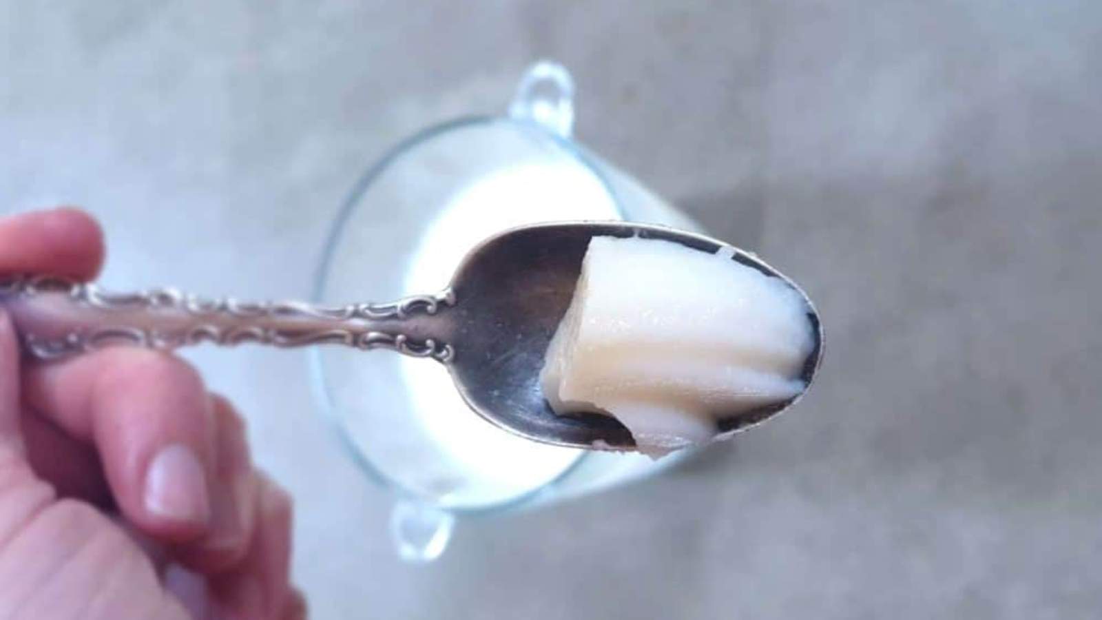 A hand holds a spoon with a bite of cheesecake pudding above a glass bowl.