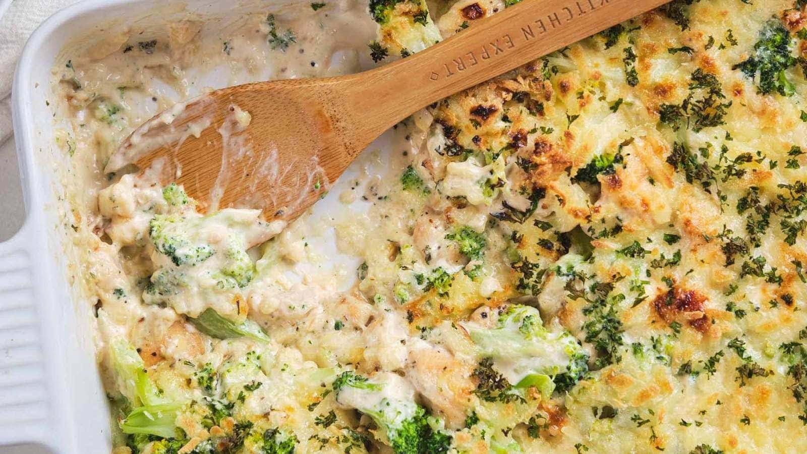 Chicken broccoli alfredo casserole, partially served with a wooden spoon in a white baking dish.