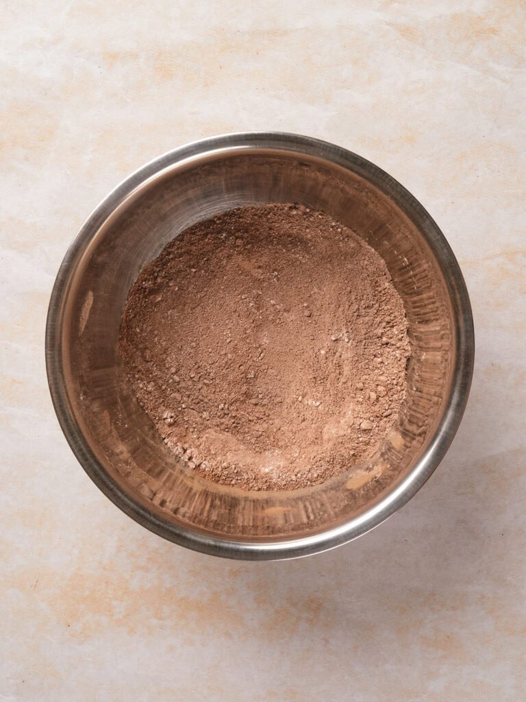 Metal bowl with brown powder inside, placed on a light stone surface.