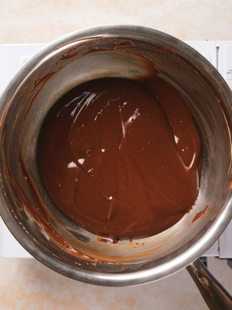 A stainless steel pot contains smooth, melted chocolate, resting on a stovetop.