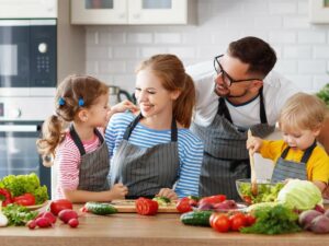 A family of four wearing aprons prepares a meal together in a kitchen.