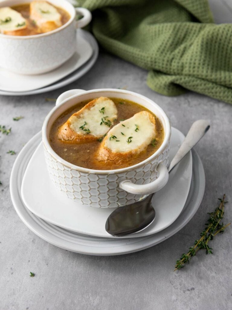 Two bowls of French onion soup topped with toasted bread and melted cheese, garnished with herbs.