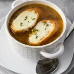 A bowl of French onion soup topped with two slices of toasted bread and melted cheese.