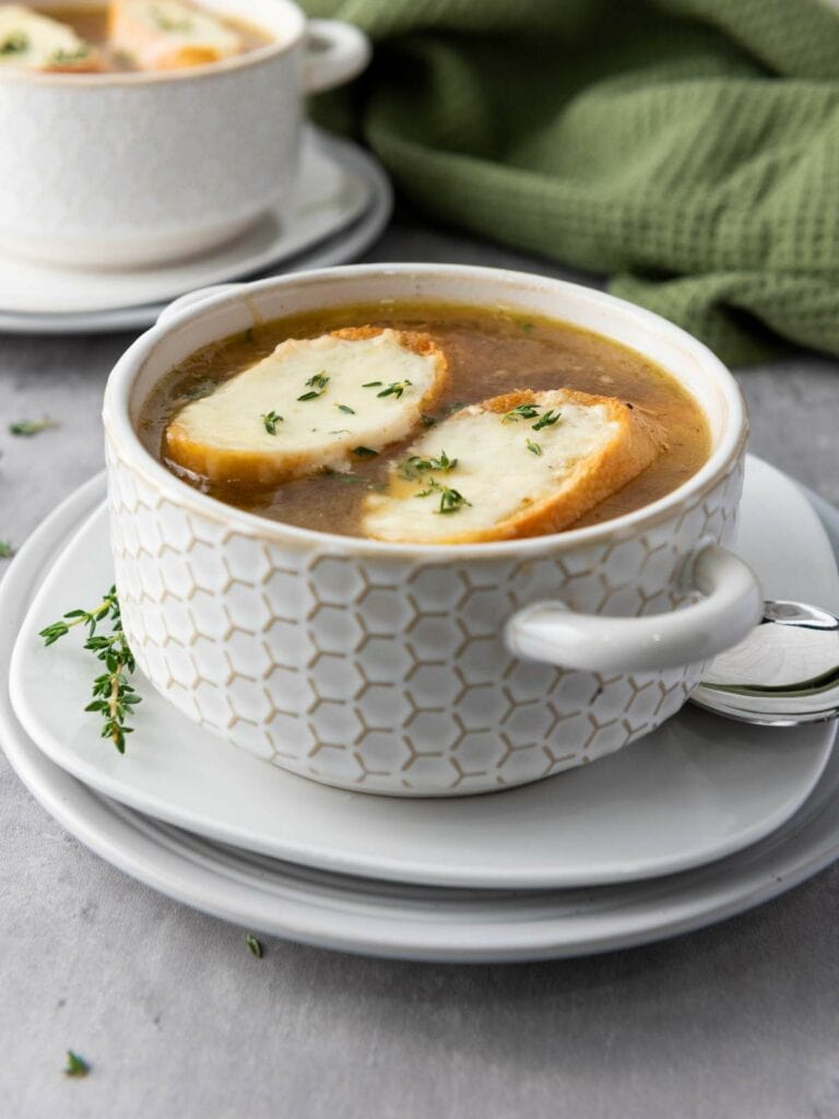 Bowl of French onion soup topped with toasted bread and melted cheese garnished with herbs.