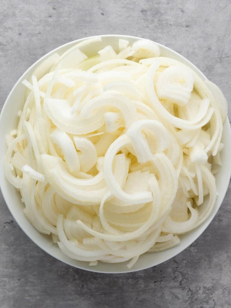 A bowl filled with thinly sliced white onions on a gray surface.