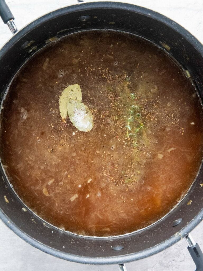 A large pot filled with simmering broth, containing a bay leaf, visible herbs, and spices.