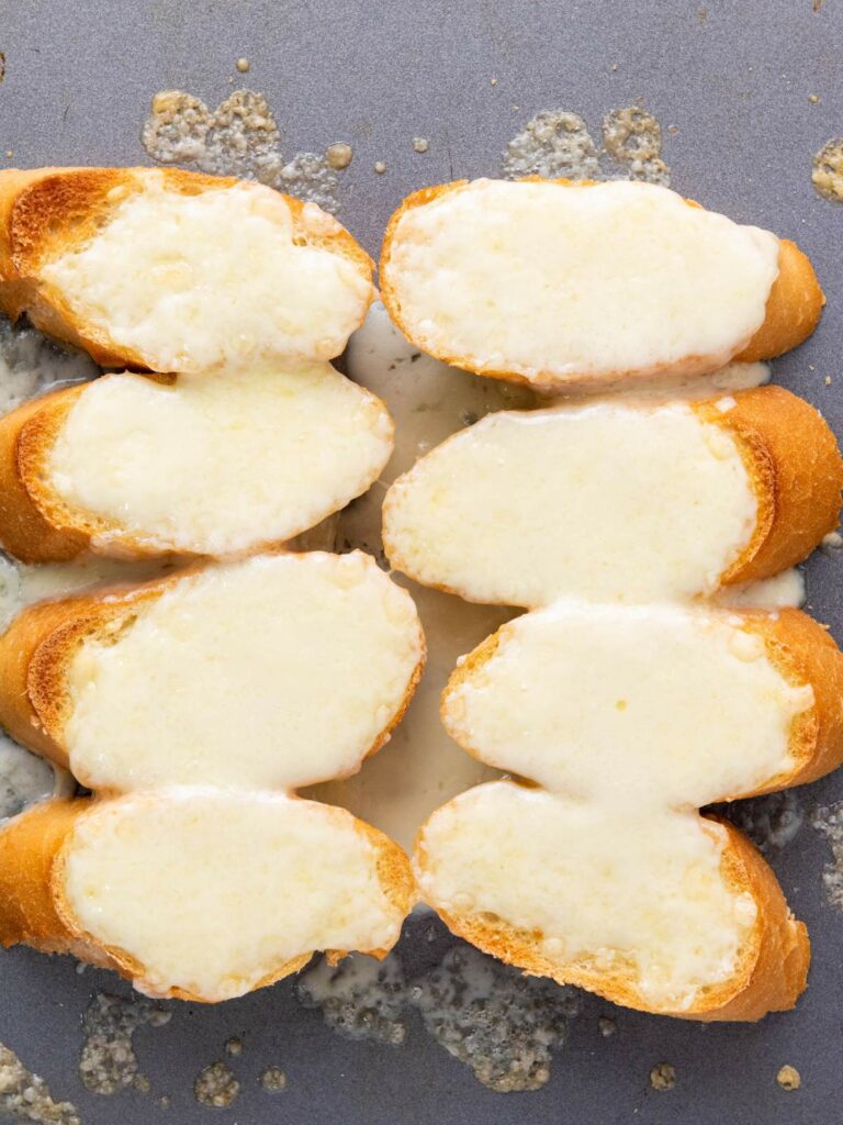 Slices of French bread topped with melted cheese on a baking sheet.