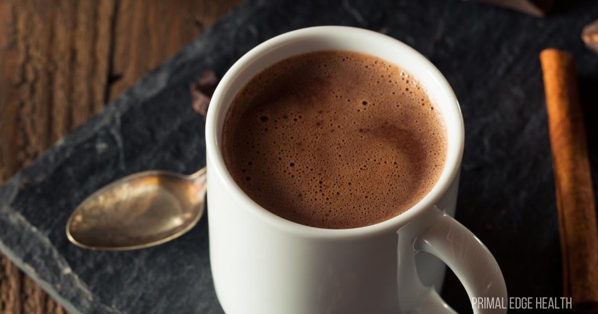 Hot chocolate in a white mug with silver spoon and ingredients around.