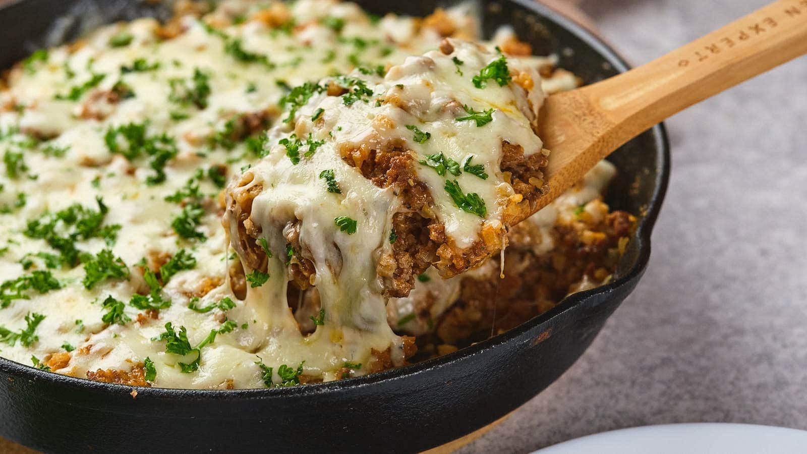 Italian ground beef skillet, garnished with parsley, being served with a wooden spoon.