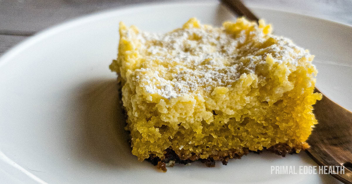 Square slice of ooey gooey butter cake on white plate with fork on the side.