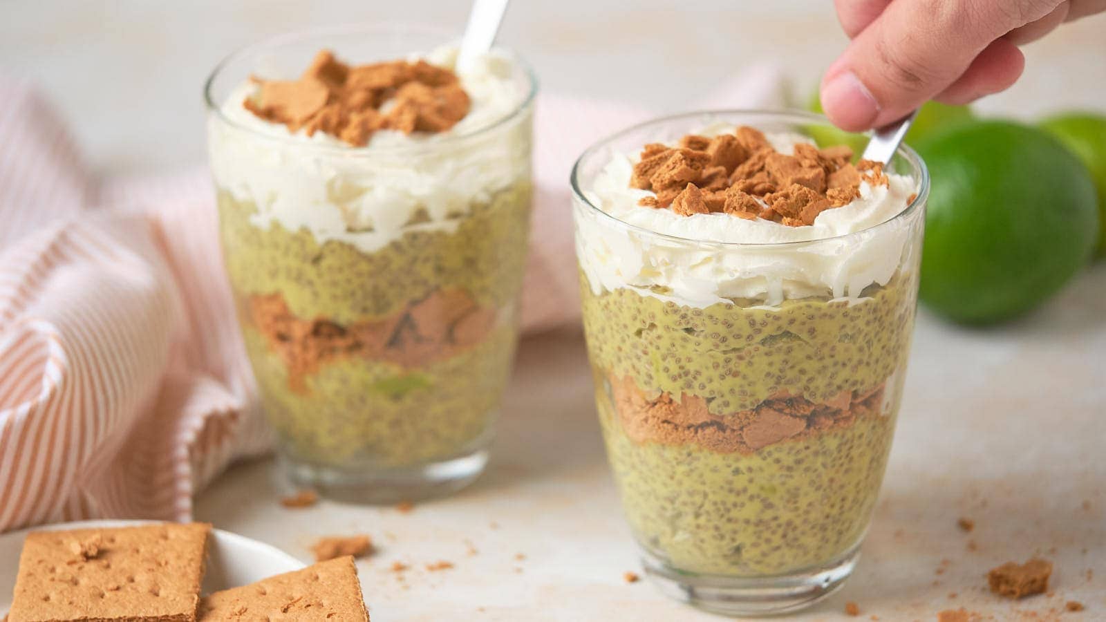 Two glasses of chia pudding topped with whipped cream and crumbled biscuits.