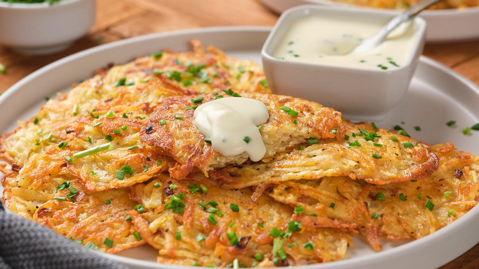 A plate of crispy potato pancakes garnished with chopped chives and a dollop of sour cream.