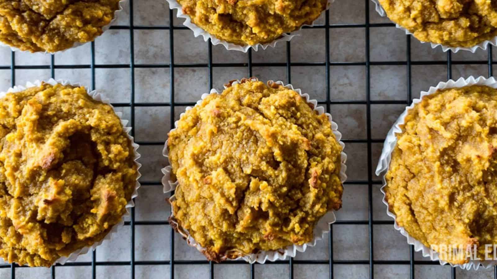 Six pumpkin muffins on a cooling rack with a grid pattern viewed from above.