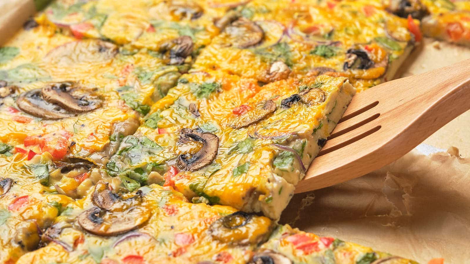 Sheet pan eggs cut into squares, served from a tray with a wooden spatula.