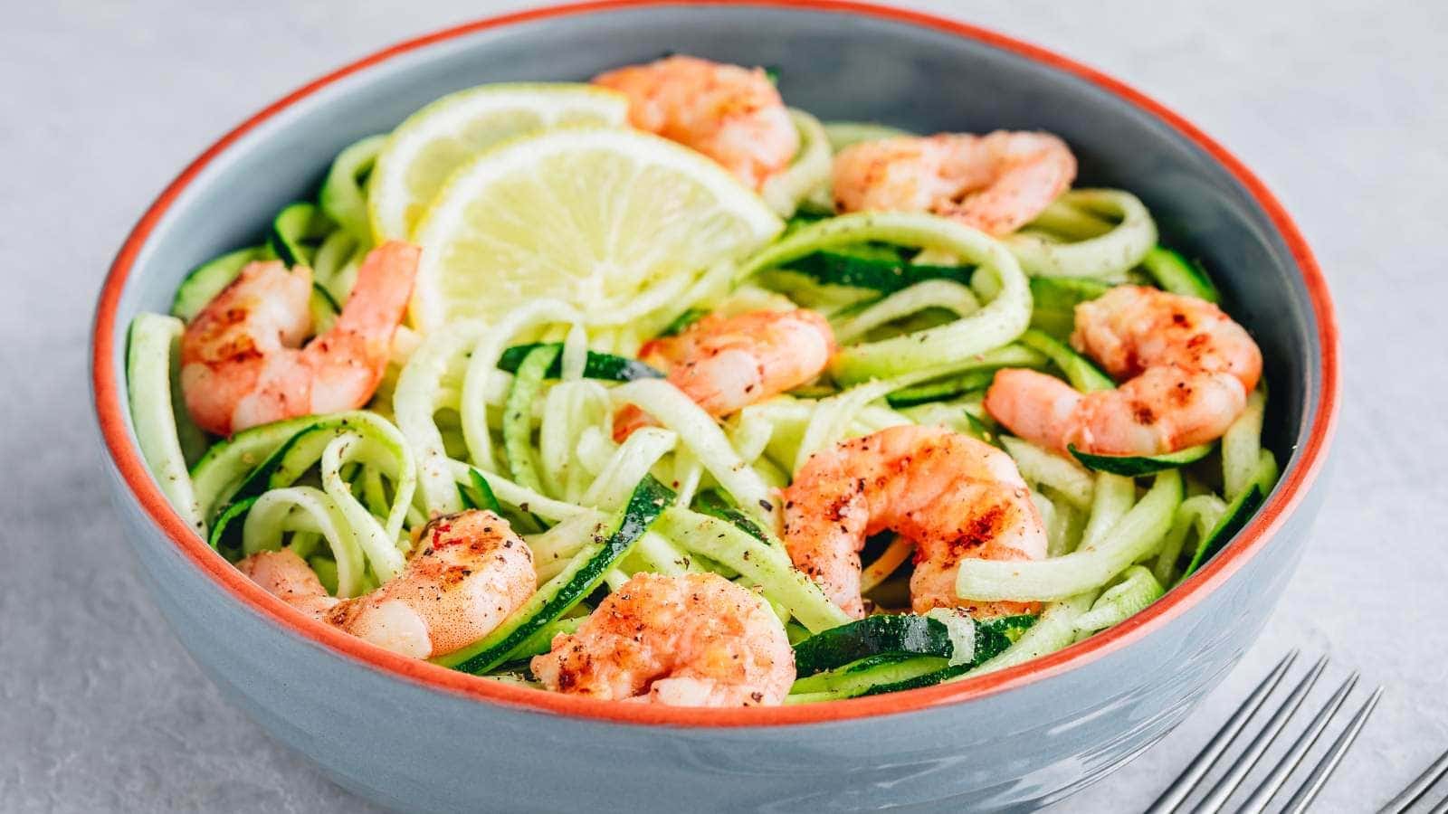 A bowl of shrimp scampi garnished with lemon slices, placed on a light grey surface next to a fork.