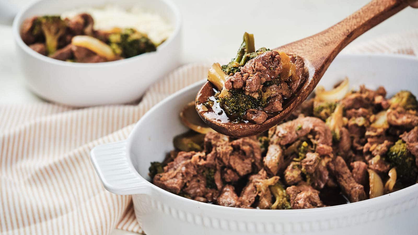 Slow cooker beef and broccoli with onion in brown bowl.