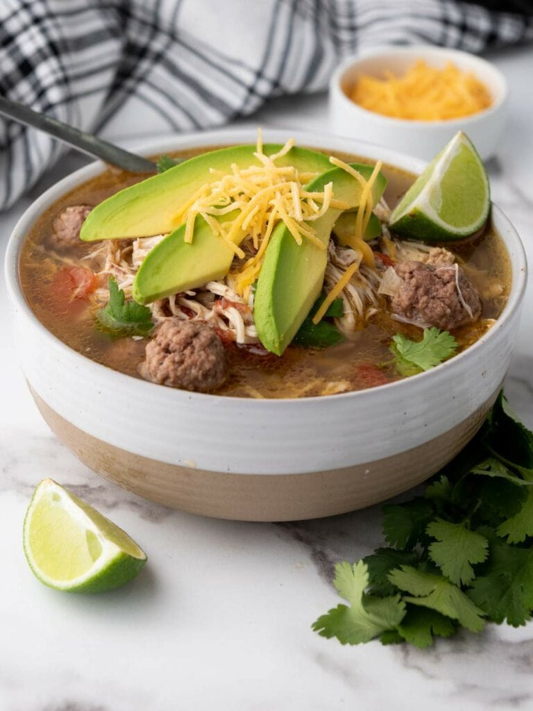 Bowl of taco soup with meatballs, shredded chicken, avocado slices, cheese, and cilantro.