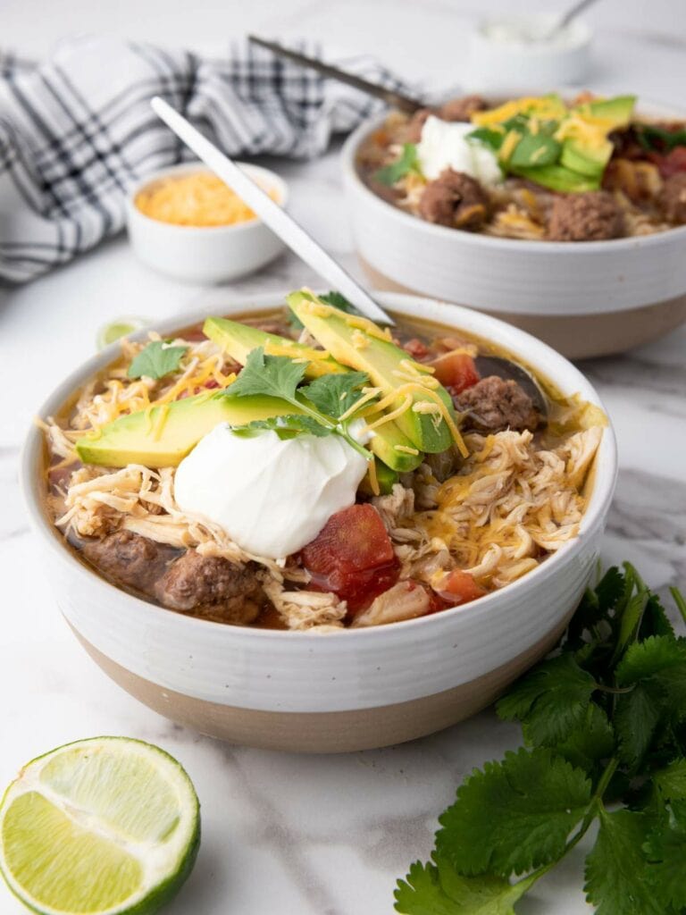 Two bowls of taco soup topped with avocado slices, sour cream, and cilantro.