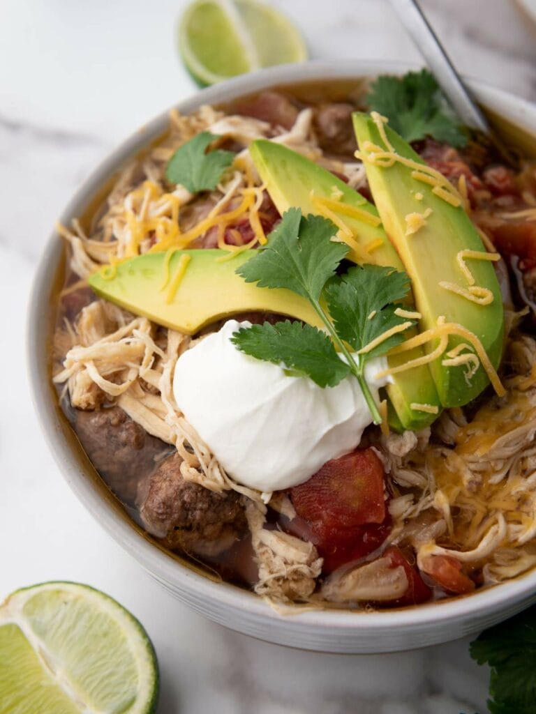 A bowl of taco soup topped with avocado slices, shredded cheese, sour cream, and cilantro.