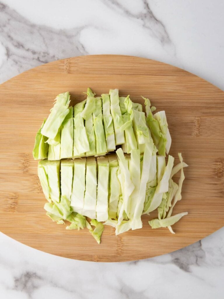 Chopped cabbage on a wooden cutting board, placed on a marble surface.