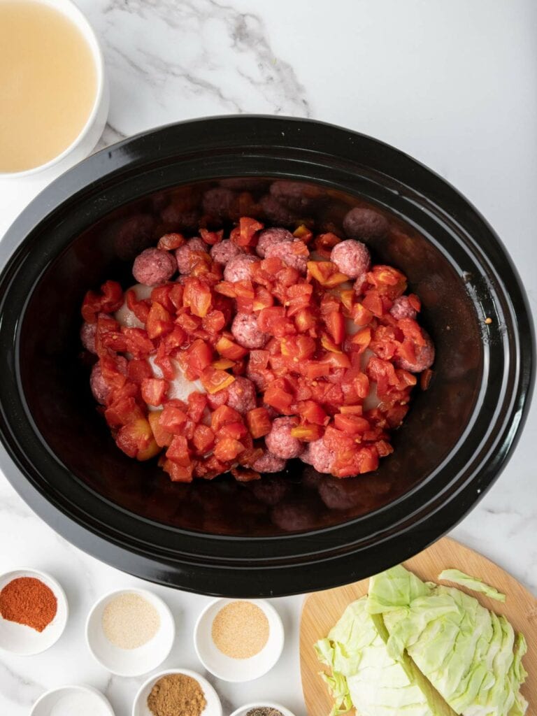 Slow cooker containing ground meat and tomatoes, surrounded by spices.