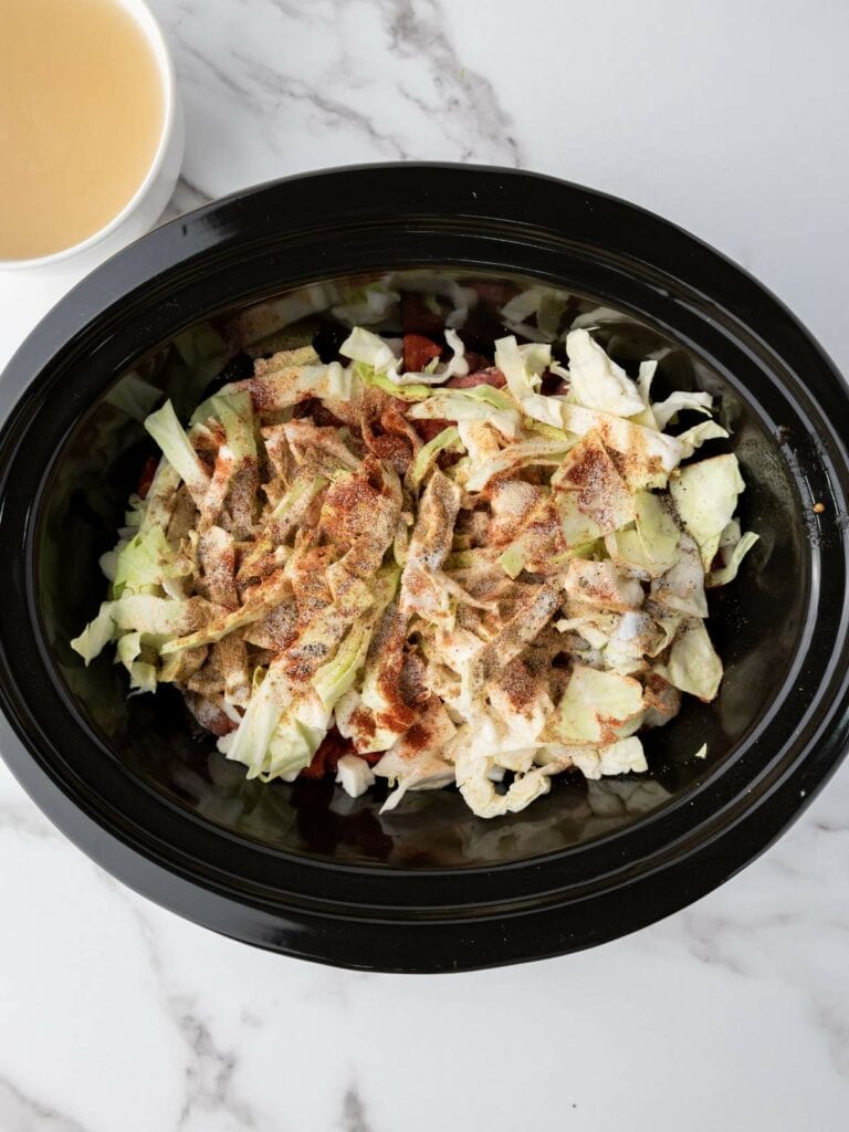 Slow cooker filled with chopped cabbage and spices.