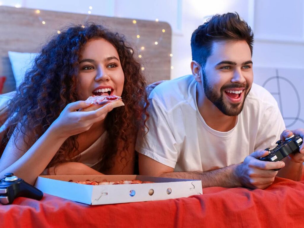 A woman eats pizza while a man plays video games.