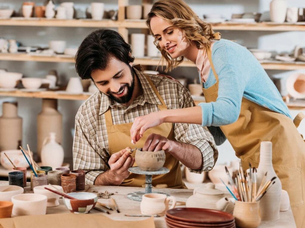 A man and a woman wearing aprons work on pottery in a studio.