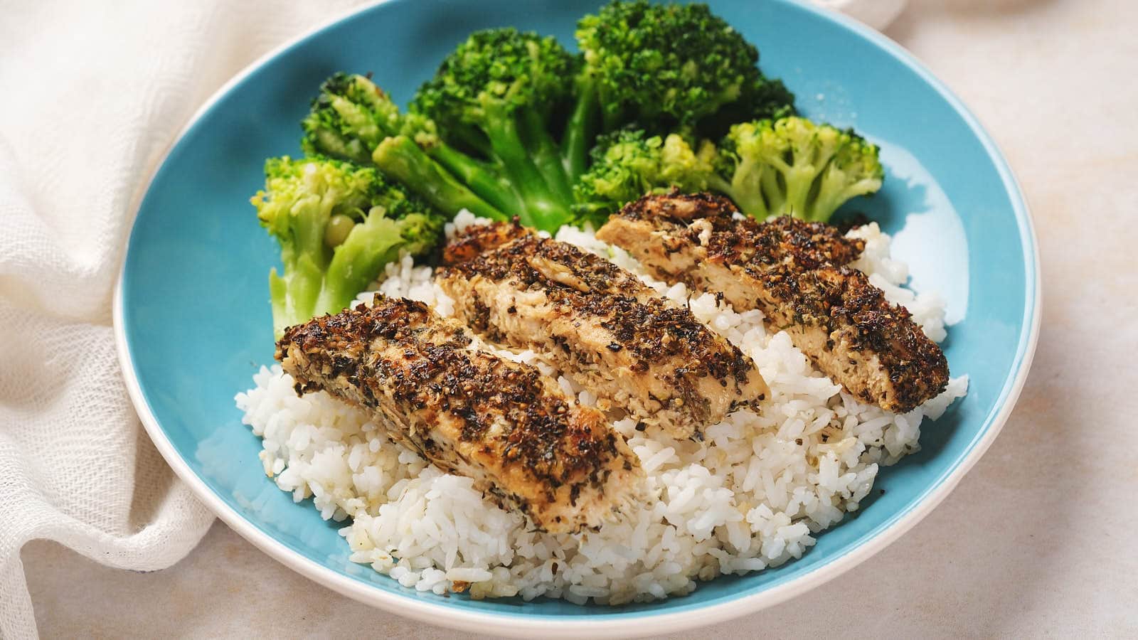 A blue plate with white rice, grilled herb-seasoned chicken slices, and steamed broccoli.