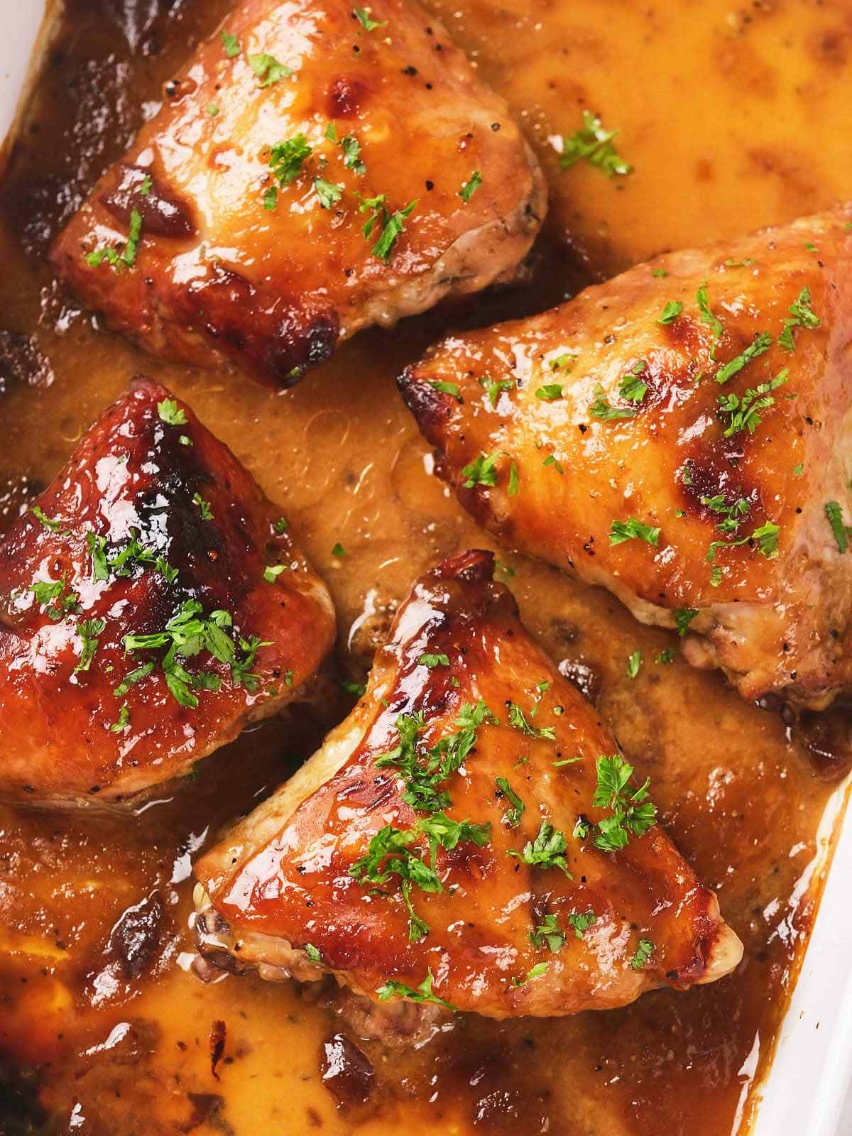 Four baked chicken thighs in apricot sauce, garnished with chopped parsley.