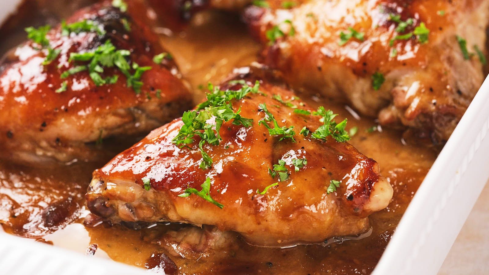 Baked apricot chicken with a golden glaze, garnished with chopped parsley, served in a white dish.