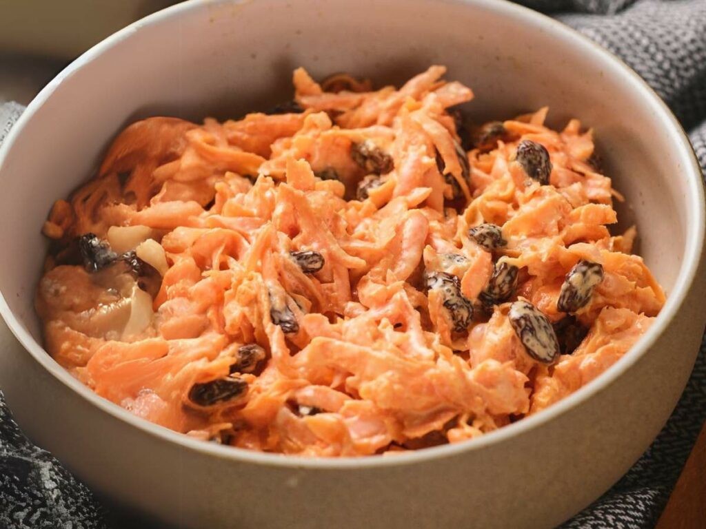 Bowl of shredded carrot salad mixed with raisins.