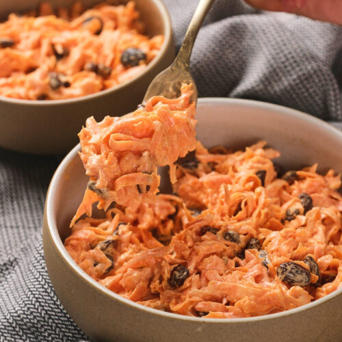 A person holding a fork with a bite of carrot raisin salad.