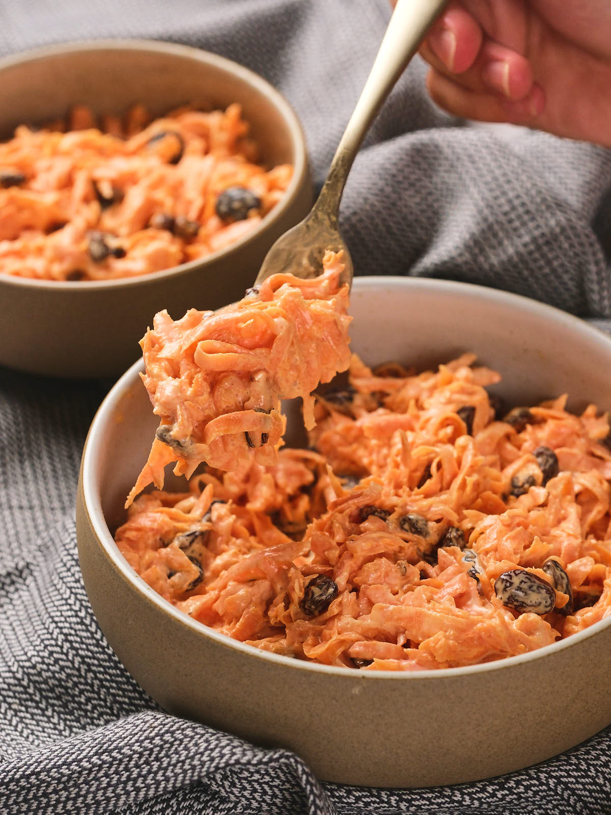 A person holding a fork with a bite of carrot raisin salad.