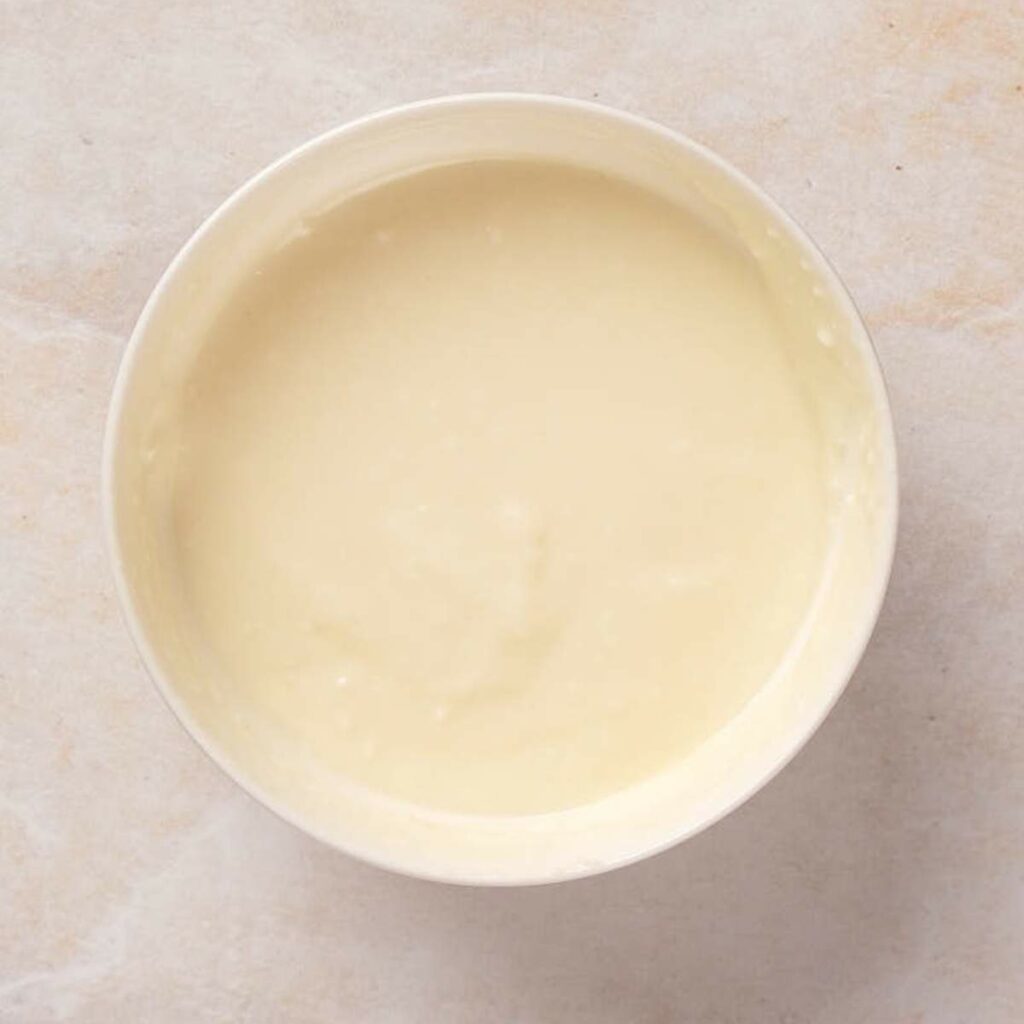 A bowl filled with creamy, light yellow batter on a textured surface.