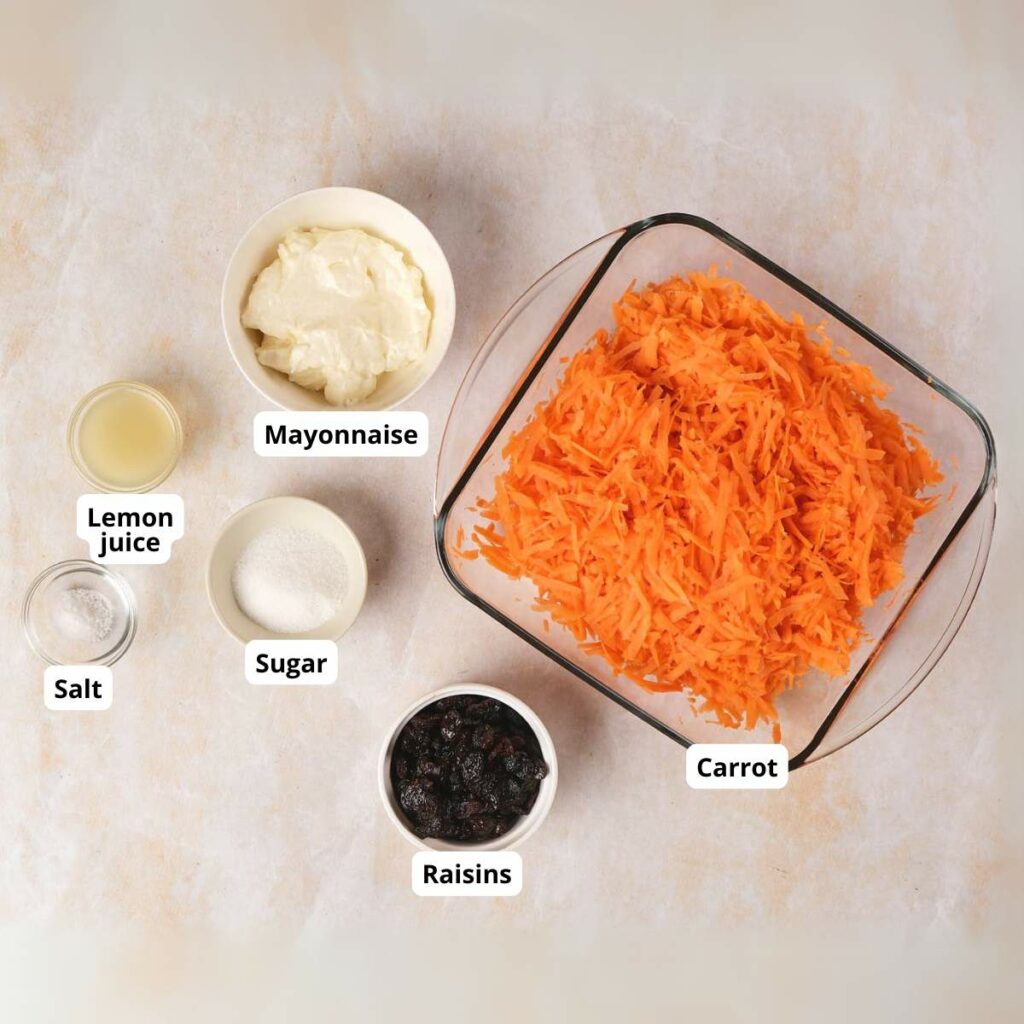 Ingredients for carrot raisin salad are arranged, all labeled.