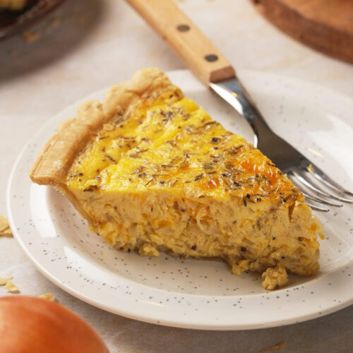 Slice of cheese and onion quiche with a golden crust and creamy filling on a speckled plate.