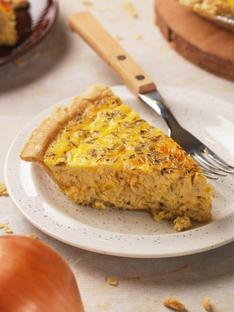 Slice of cheese and onion quiche with a golden crust and creamy filling on a speckled plate.