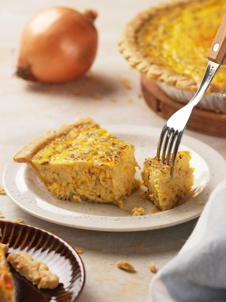 A fork lifting a piece of cheese and onion quiche on a white plate.