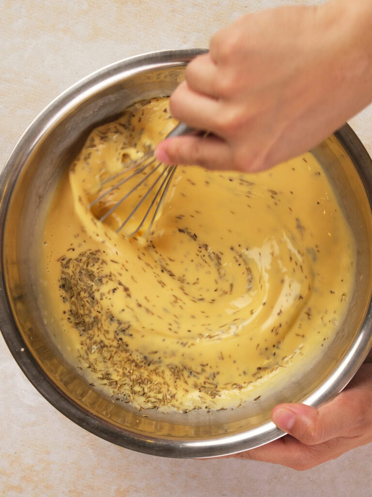 Hands whisking yellow liquid with seeds in a metal bowl.