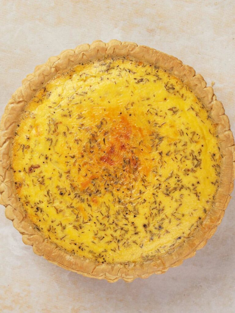 Top view of a whole quiche with a golden crust and visible herbs on the surface.