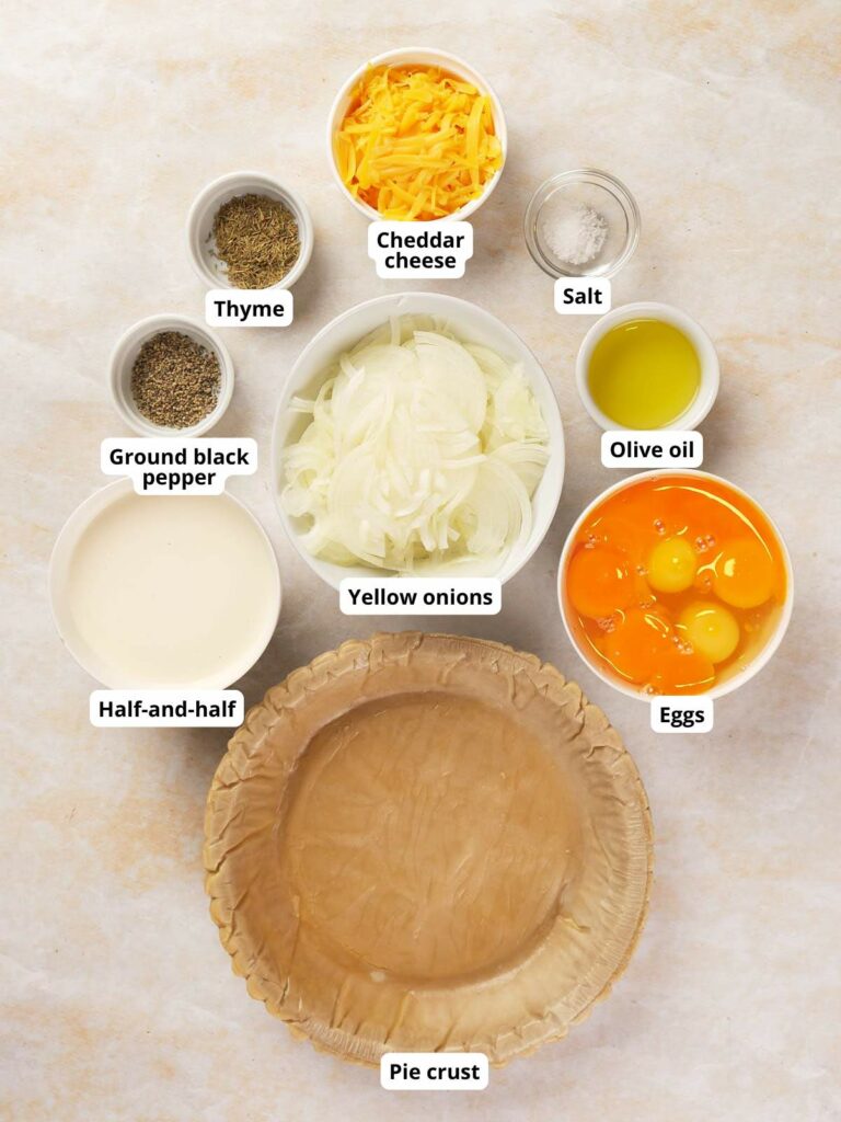 Ingredients for a cheese and onion quiche on a light colored surface, each labeled.