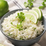 A bowl of chipotle rice garnished with cilantro and lime slices, placed on a cloth.