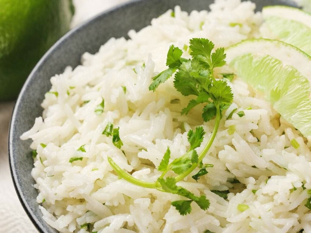 A close-up of a bowl of chipotle rice garnished with cilantro and lime slices.