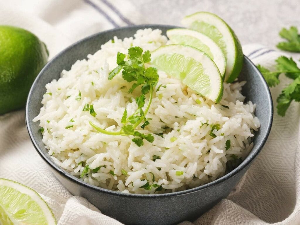 A bowl of chipotle rice garnished with cilantro and lime slices, placed on a cloth napkin.