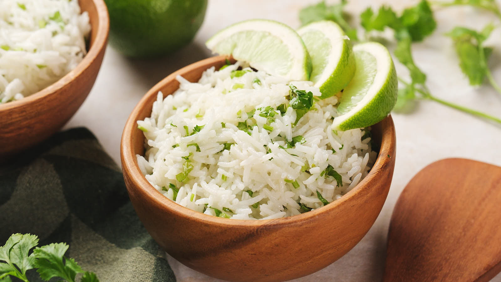 A wooden bowl filled with cilantro lime rice garnished with chopped herbs and lime wedges.