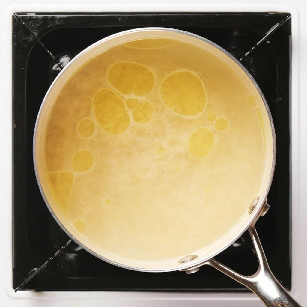 Pot of yellow liquid with oil droplets sits on a black stovetop.