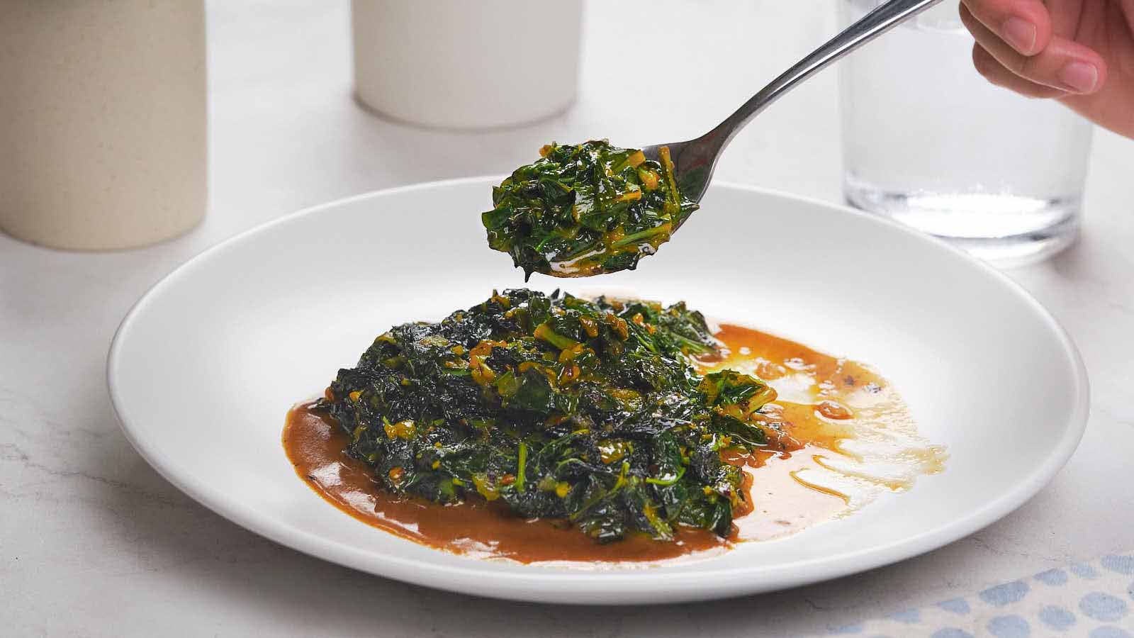 A plate of sautéed leafy greens in sauce, with a fork holding a portion above the dish.