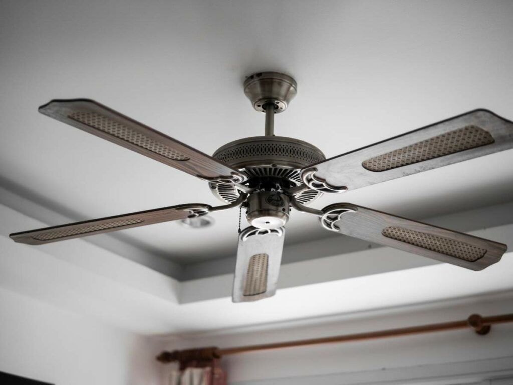 A ceiling fan with four metal blades and a metallic finish is mounted on a white ceiling.