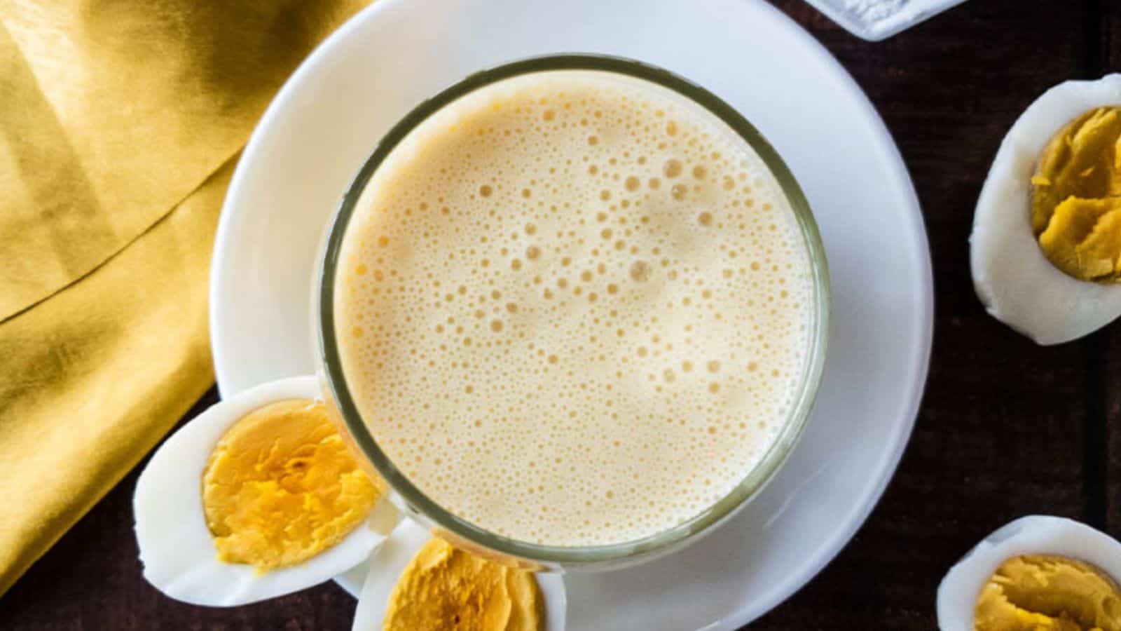 High-protein smoothie in glass on white saucer with hard boiled eggs cut in half.